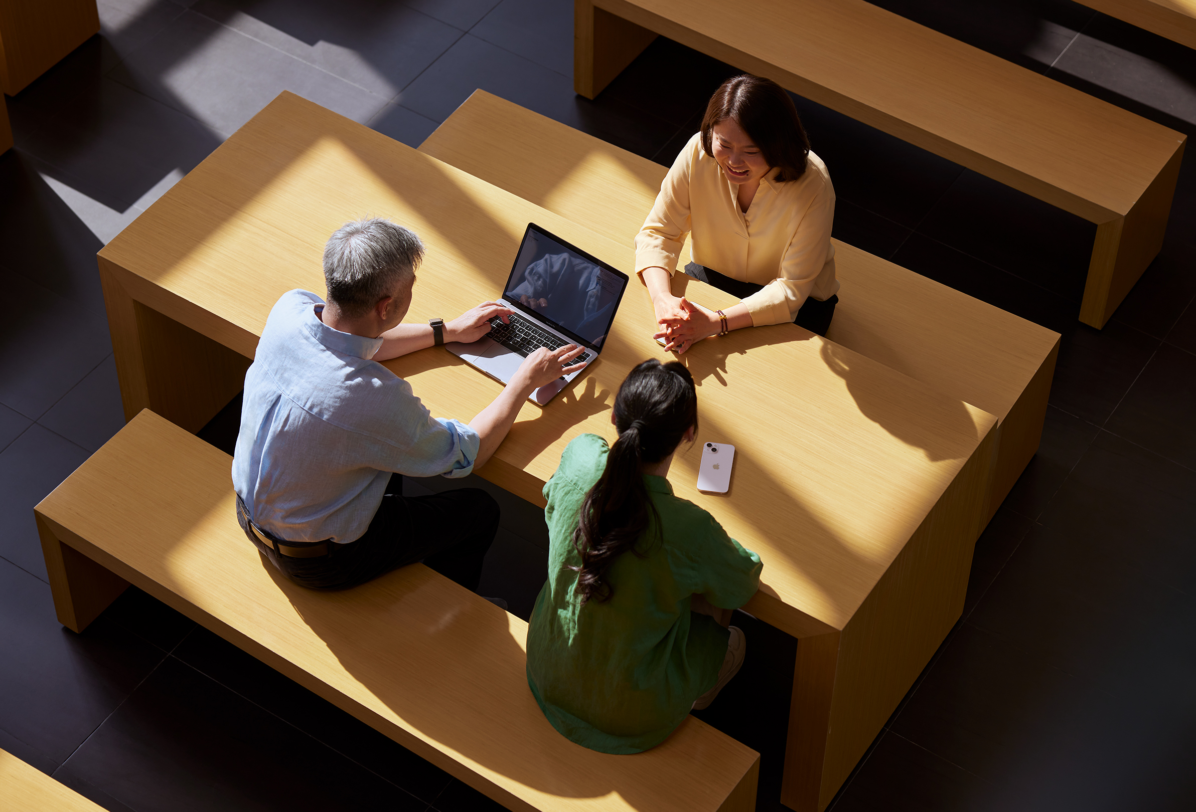 Trois membres de l’équipe Apple installés autour d’une table dont l’un travaille sur un MacBook.