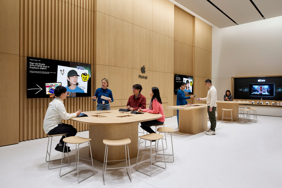 Clientes sentados en una mesa de Today at Apple dentro de la tienda.