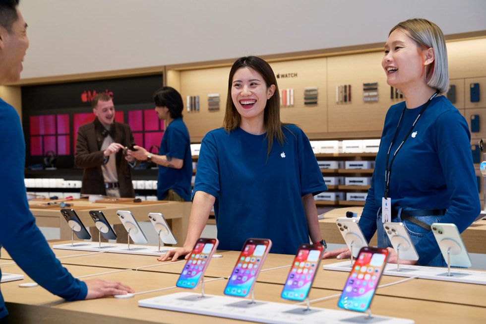 Tres integrantes del equipo de pie alrededor de una mesa que muestra la última familia del iPhone.