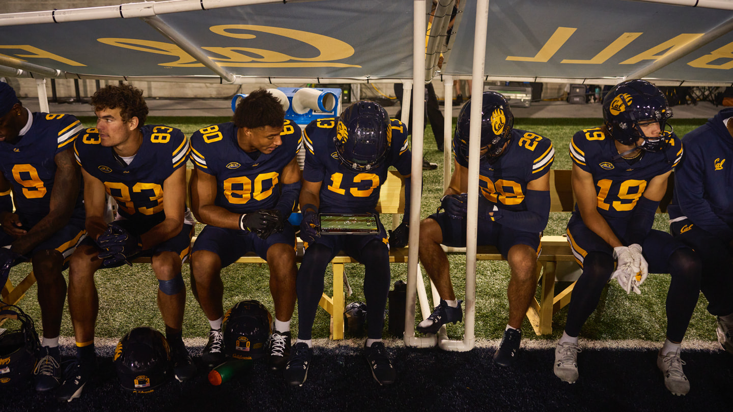 Cal teammates sit on the bench during a football game and review footage on iPad?Pro.