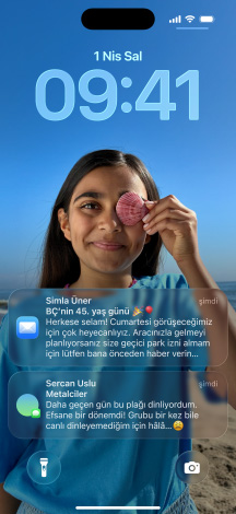 Hafif?e birbirinin üstüne binen be? iPhone modeli; en soldaki ekran, arka plan? ki?iselle?tirilmi? bir Mesajlar sohbetini g?steriyor; soldan ikinci modelin ekran?nda renkli uygulama simgelerinin bulundu?u Ana Ekran g?rünüyor; ortadaki modelde, foto?rafl? Kilit Ekran? ve Liquid Glass efektiyle saat rakamlar? g?rünüyor, ekran?n alt?nda iki bildirim yer al?yor; sa?dan ikinci modelde Liquid Glass efektli ?effaf uygulama simgeleri g?rünüyor; en sa?daki modelde ise Liquid Glass tasar?m?nda bir müzik ?alar yer al?yor