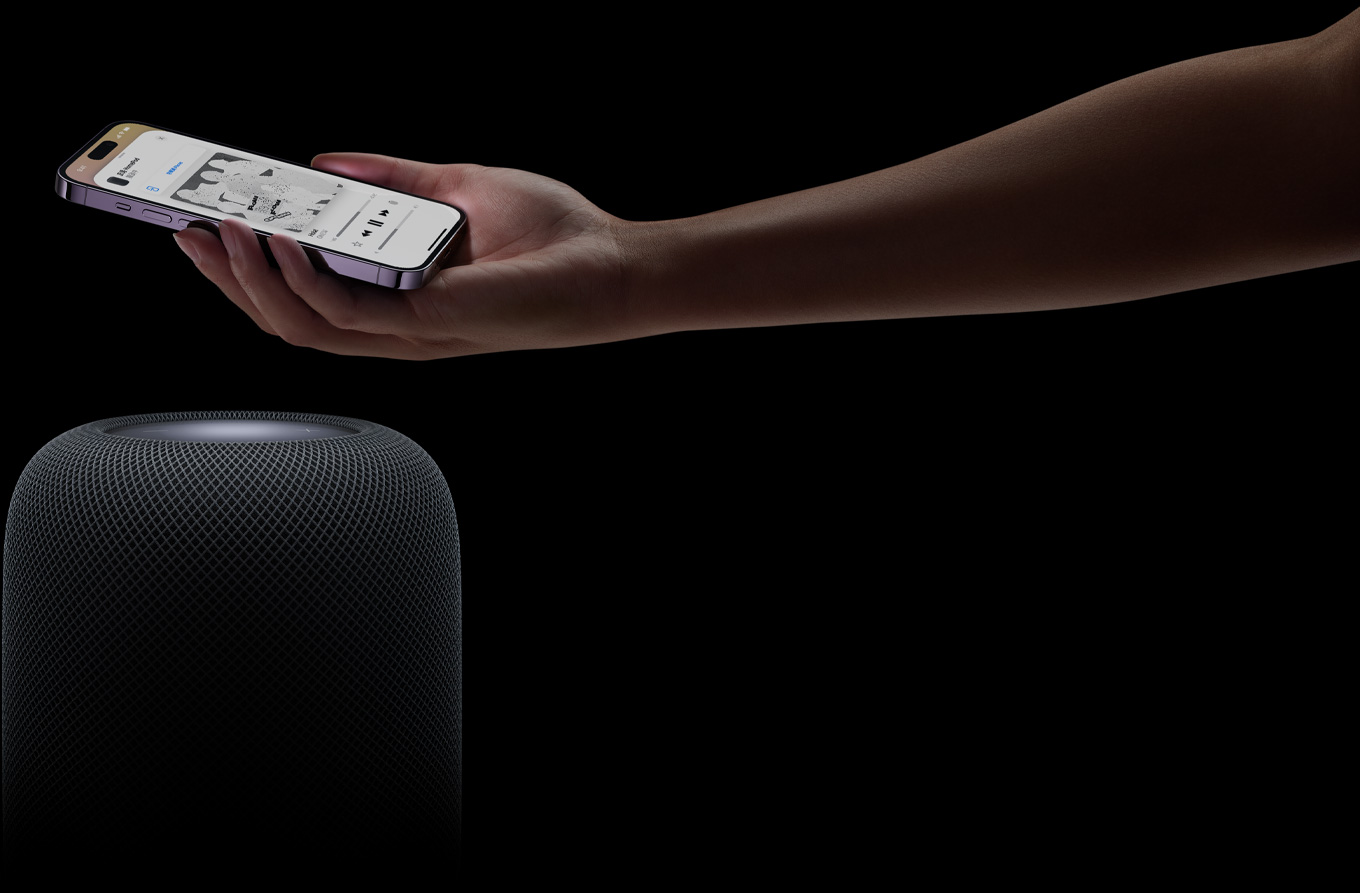 從頁面右側(cè)伸入的手拿著 iPhone 舉放在 HomePod 揚聲器上方