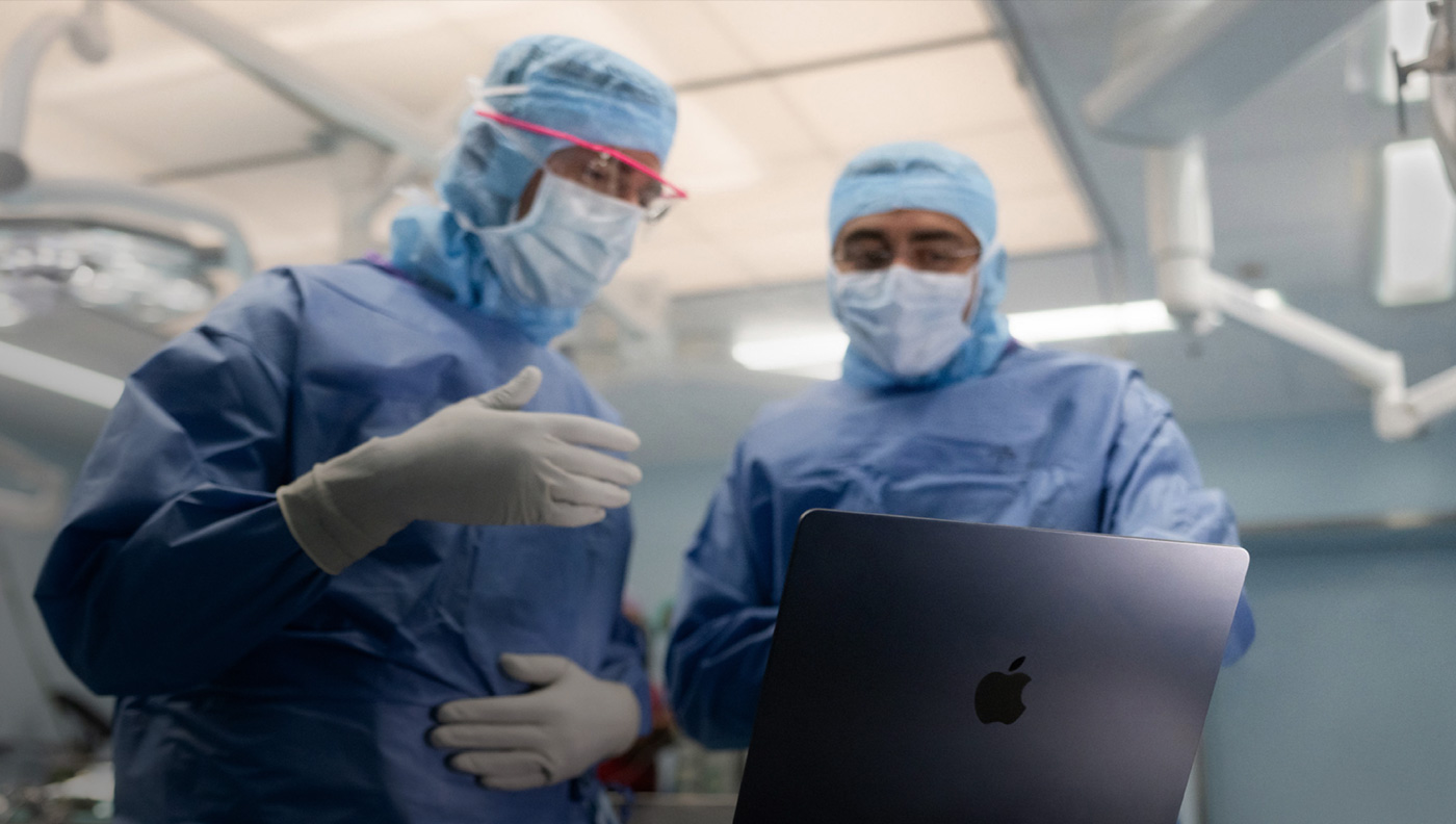 Two surgeons discussing something on the screen of a MacBook Pro in the operating room.
