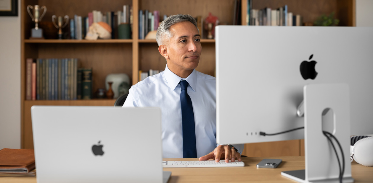 M?t nhan viên y t? ng?i ? bàn làm vi?c, ?ang nhìn vào iMac và MacBook Pro.